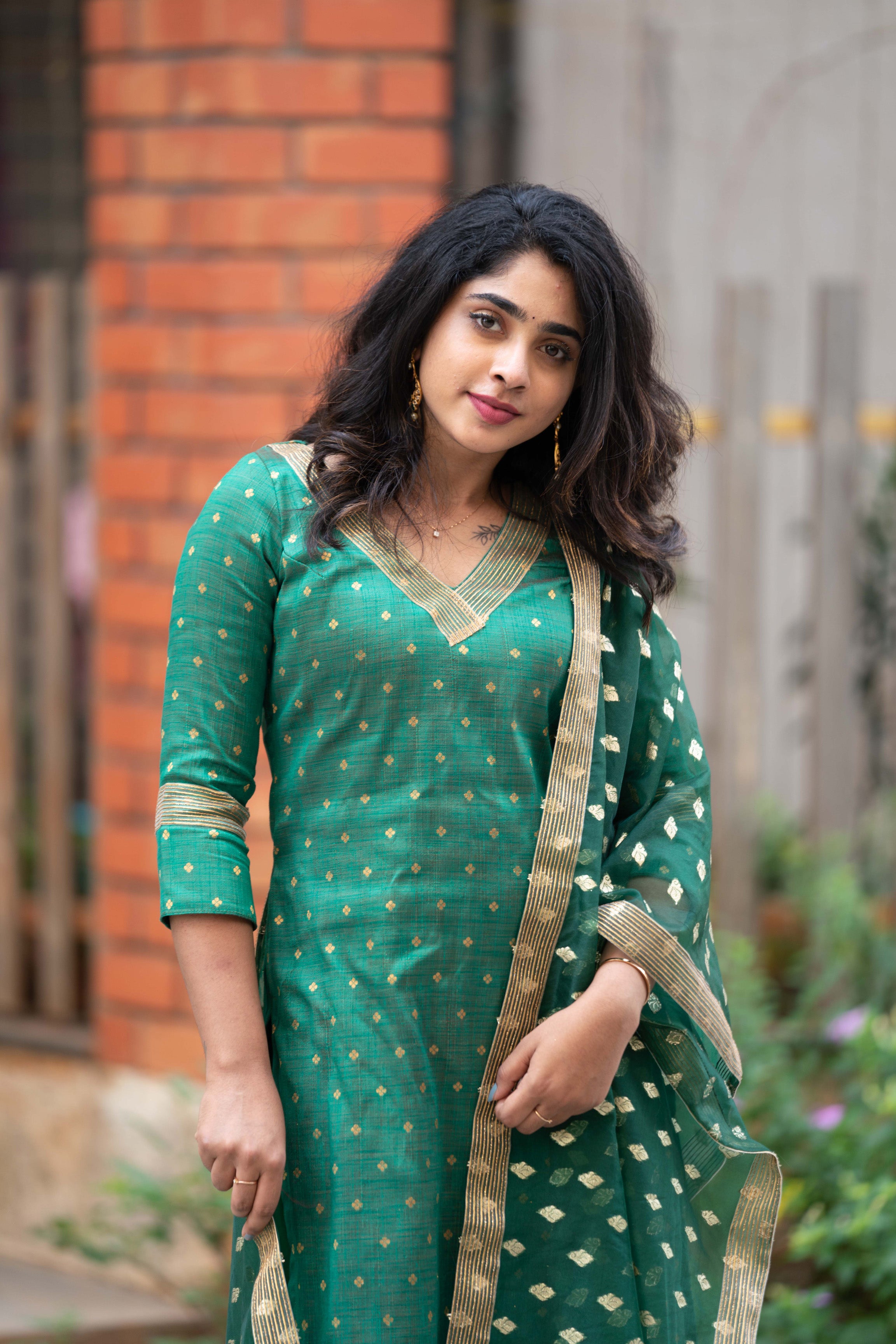 A stunning green brocade raw silk kurti for women featuring zari motifs, lace detailing, and an organza dupatta. Branded designer straight kurta with a deep V-neck.